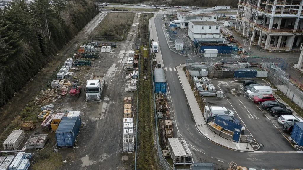 Magasból fotózott építési terület rendezett és kevésbé rendezett logisztikai zónákkal, útvonalakkal, depókkal és parkolóval.